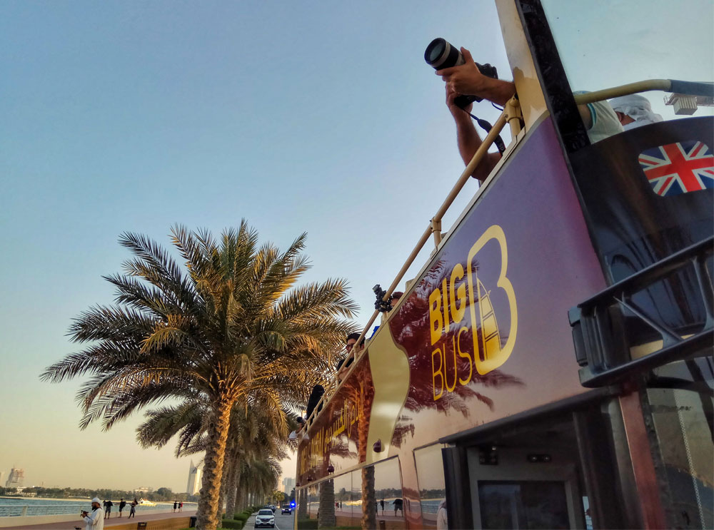 Passagier macht Foto von der Big Bus Tour mit offenem Verdeck in Dubai, während die Sonne untergeht