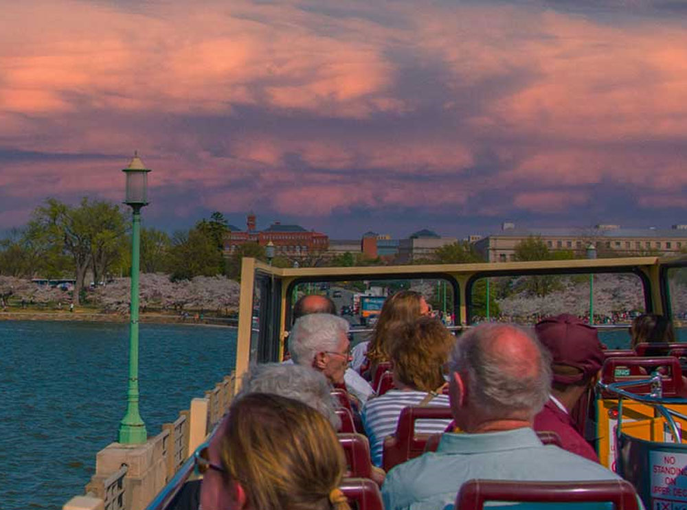 Passengers on the top deck of a tour bus at sunset