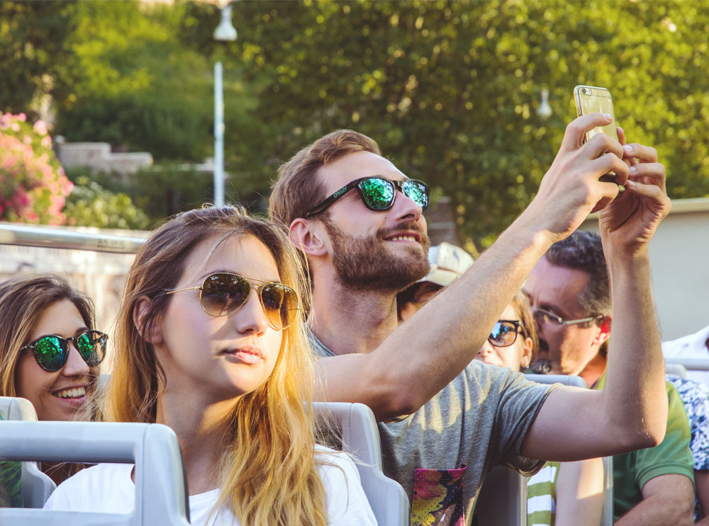 Man taking photo on phone on top deck of tour bus