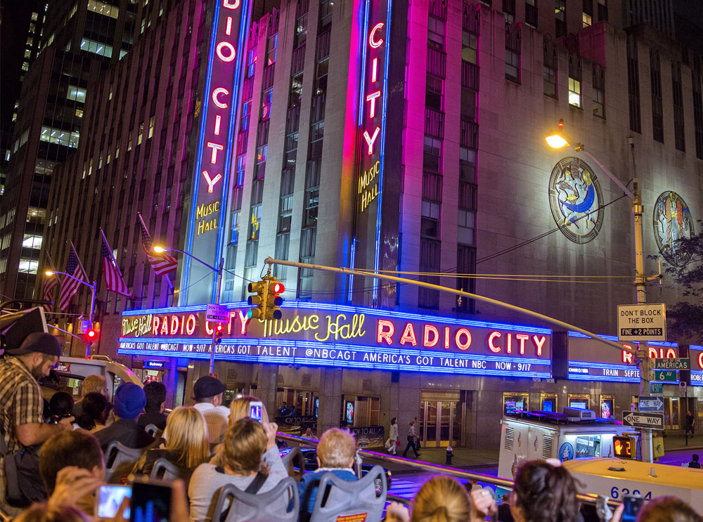 Big Bus sightseeing tour passing Radio City Hall at night
