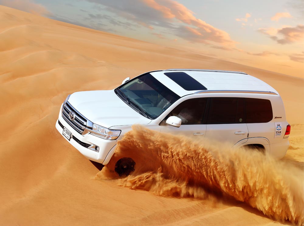 A Tour Dubai Toyota Landcruiser drives through the desert leaving a sandy wake