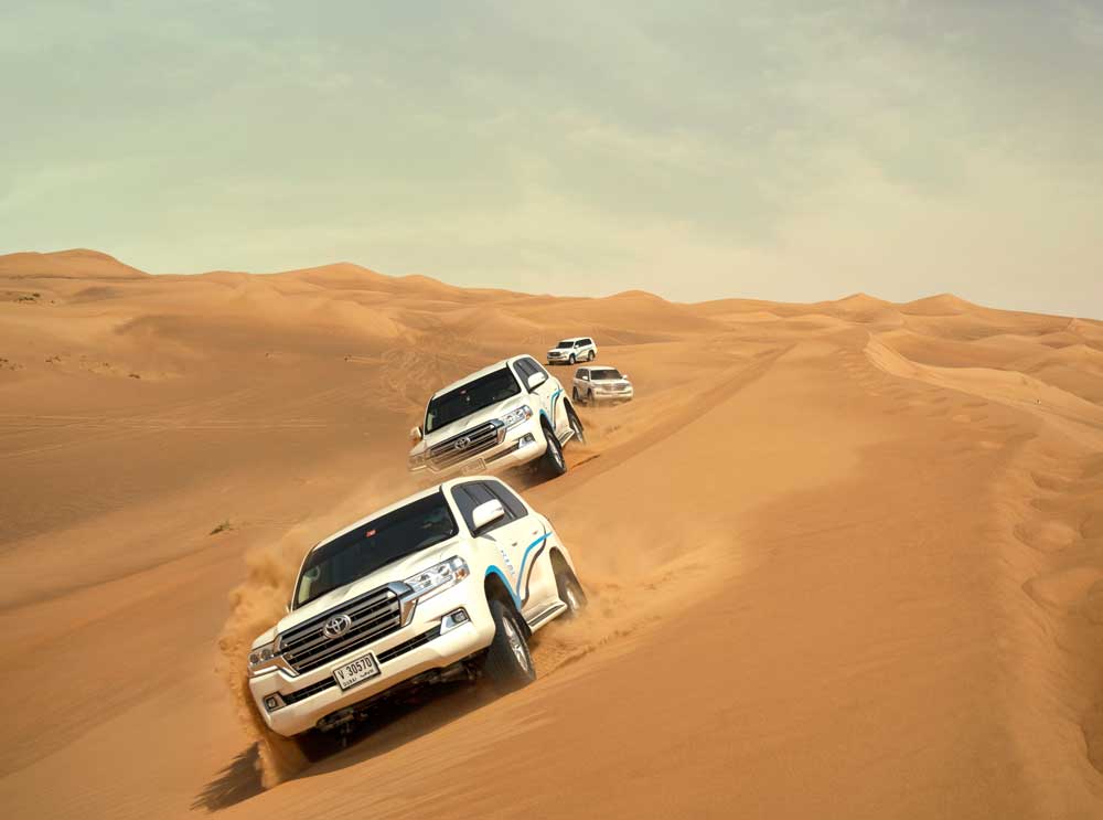 Four white Toyota Landcruisers charge through the desert